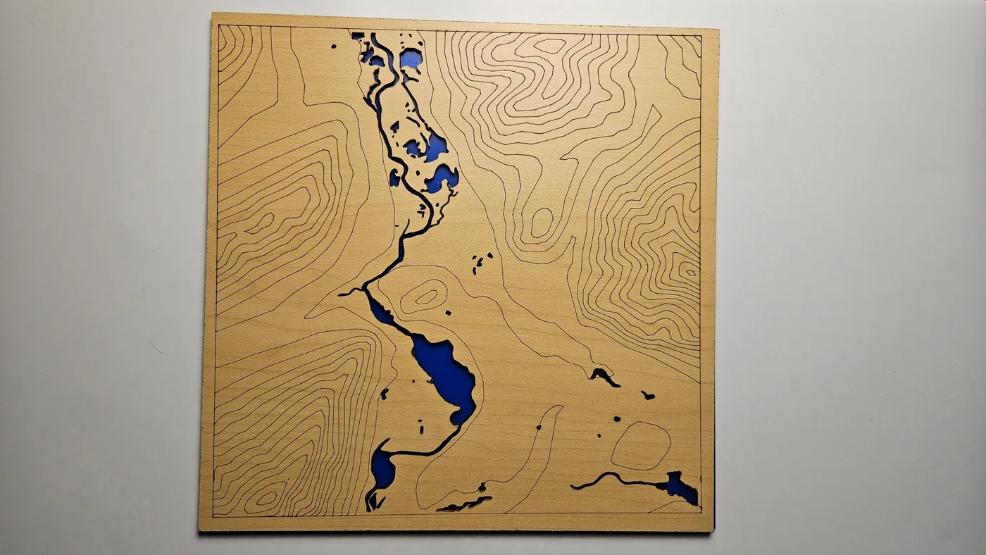 A wooden panel with scored elevation contour lines and a blue river cut through it